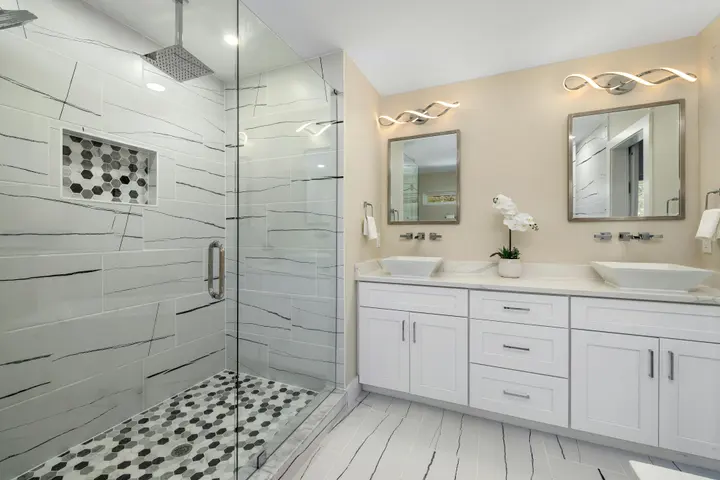 Double vanity with vessel sinks beside a glass shower with a hexagon mosaic floor
