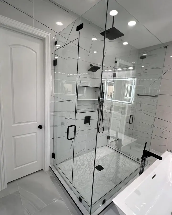 Frameless glass shower enclosure with matte black hardware and large-format veined tile