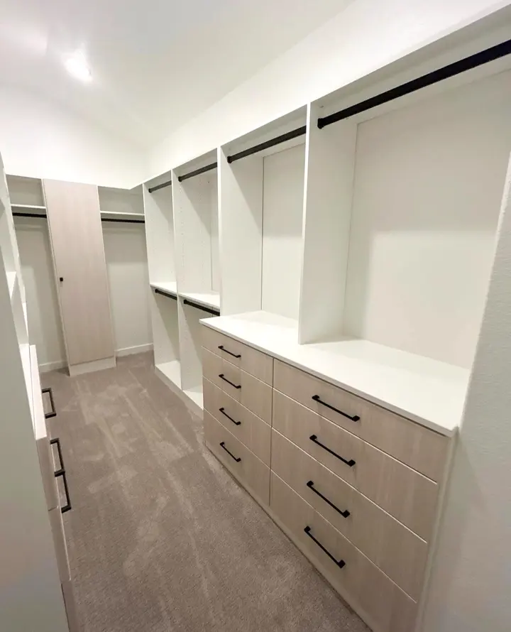 Walk-in closet with light oak drawer fronts, matte black pulls and white shelving