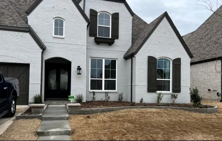 Brick house painted white with dark shutters, dark front doors and a matching garage door