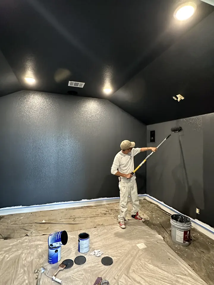 Painter rolling a deep navy color onto the walls of a media room, floor protected with paper